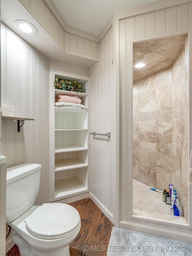 bathroom with toilet, wood finished floors, and tiled shower