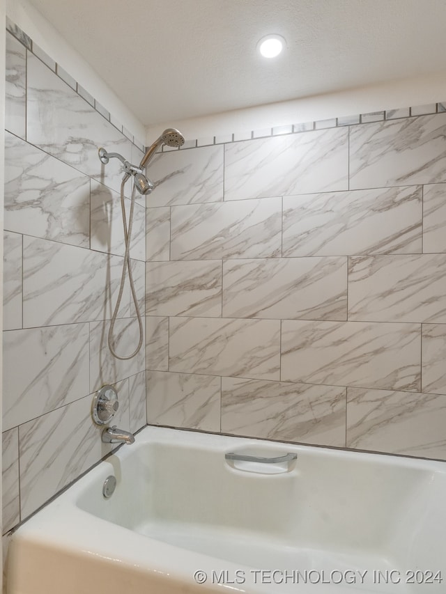 bathroom with a textured ceiling and tiled shower / bath combo