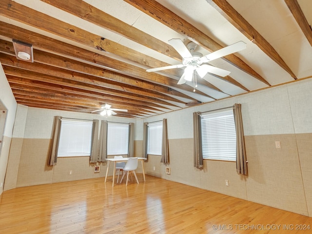 unfurnished room featuring plenty of natural light, ceiling fan, beam ceiling, and wood finished floors