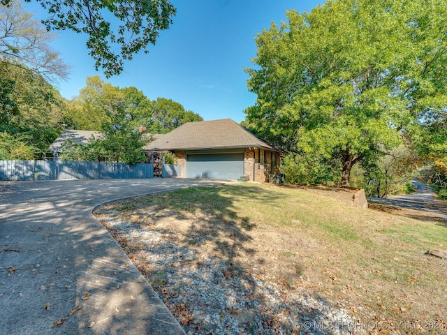 view of side of property featuring an attached garage, aphalt driveway, brick siding, fence, and a lawn