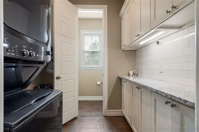 interior space featuring backsplash, stacked washer and clothes dryer, light stone countertops, dark hardwood / wood-style floors, and white cabinets