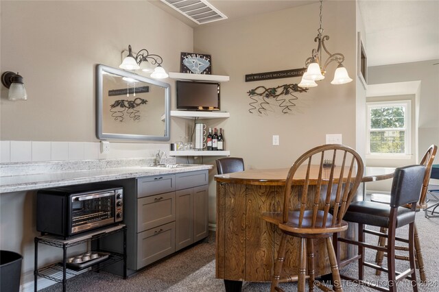 bar with pendant lighting, light stone counters, gray cabinetry, and dark colored carpet