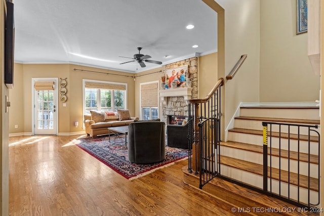 living room with ceiling fan, hardwood / wood-style floors, ornamental molding, and a stone fireplace