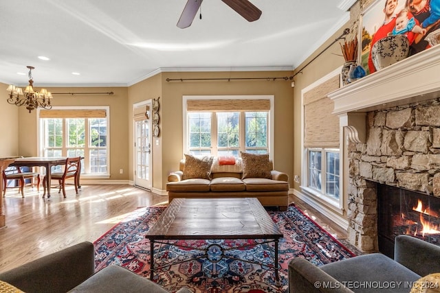 living room with ceiling fan with notable chandelier, a stone fireplace, light hardwood / wood-style flooring, and ornamental molding