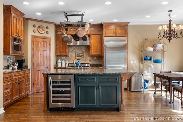 kitchen featuring stainless steel appliances, dark stone countertops, wine cooler, and a kitchen island with sink