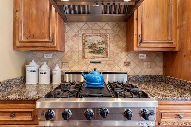 kitchen with stainless steel stove, wall chimney exhaust hood, backsplash, and dark stone countertops