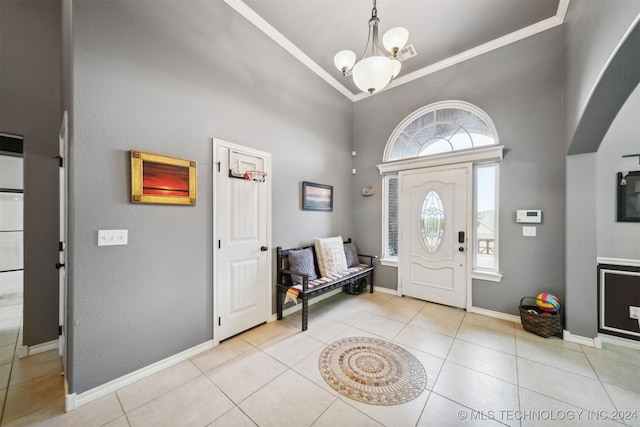 foyer with light tile patterned flooring, crown molding, a towering ceiling, and an inviting chandelier