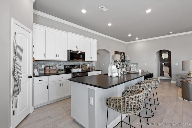 kitchen featuring a kitchen island with sink, white cabinets, black electric range oven, crown molding, and a kitchen bar