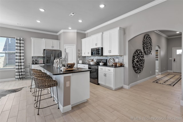 kitchen with stainless steel appliances, white cabinets, ornamental molding, a center island with sink, and a kitchen breakfast bar