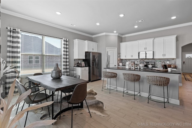 kitchen featuring light hardwood / wood-style flooring, backsplash, white cabinetry, appliances with stainless steel finishes, and a breakfast bar area