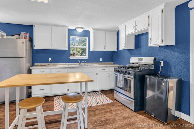 kitchen with sink, a textured ceiling, white cabinetry, appliances with stainless steel finishes, and dark hardwood / wood-style floors