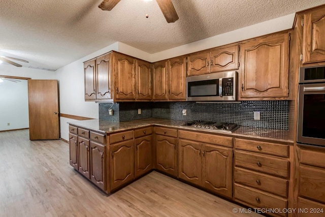 kitchen featuring light wood-type flooring, ceiling fan, decorative backsplash, appliances with stainless steel finishes, and a textured ceiling