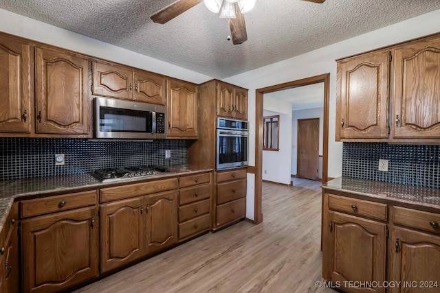 kitchen with a textured ceiling, stainless steel appliances, decorative backsplash, and light hardwood / wood-style flooring