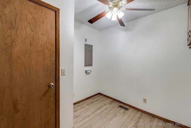 empty room featuring electric panel, ceiling fan, light hardwood / wood-style flooring, and a textured ceiling