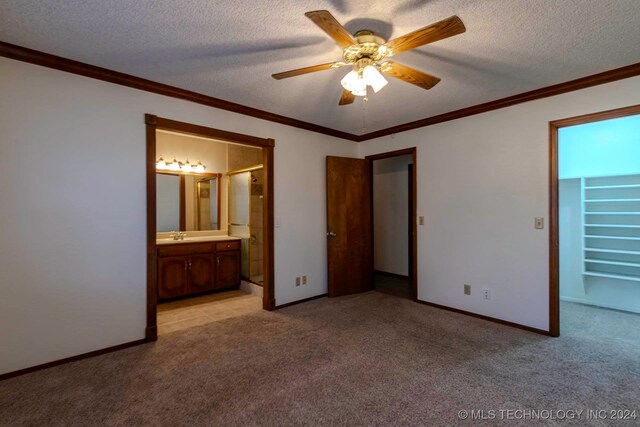 unfurnished bedroom featuring ceiling fan, light colored carpet, a textured ceiling, and ensuite bath