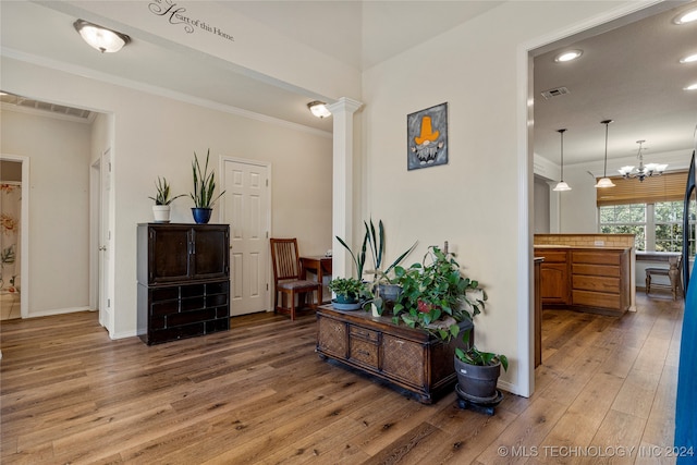 hall featuring an inviting chandelier, crown molding, hardwood / wood-style floors, and decorative columns