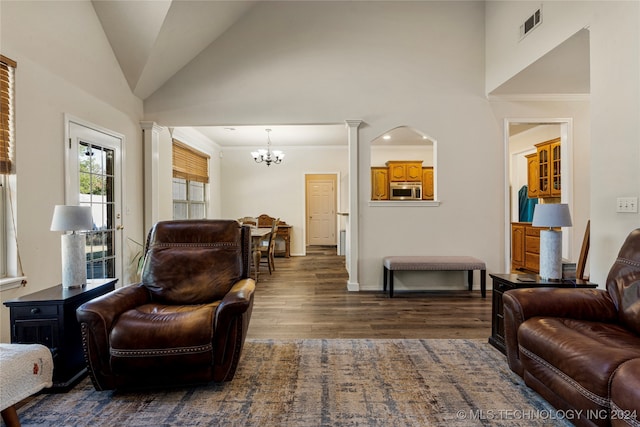 living room featuring dark hardwood / wood-style floors, high vaulted ceiling, a notable chandelier, and decorative columns