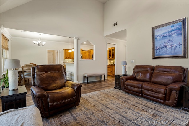 living room featuring decorative columns, a notable chandelier, dark hardwood / wood-style floors, and a high ceiling