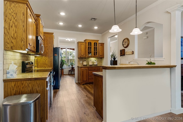 kitchen featuring wood-type flooring, decorative light fixtures, kitchen peninsula, ornamental molding, and appliances with stainless steel finishes