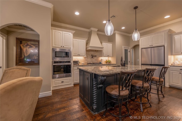 kitchen featuring dark hardwood / wood-style flooring, stainless steel appliances, an island with sink, white cabinets, and custom exhaust hood