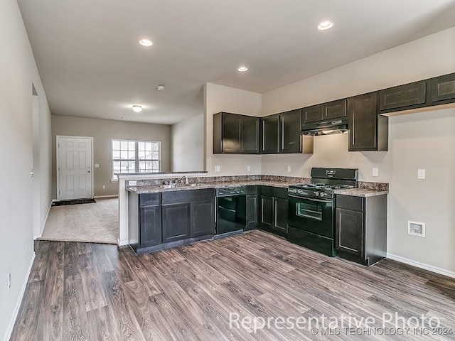 kitchen with light stone counters, sink, kitchen peninsula, light hardwood / wood-style flooring, and black appliances