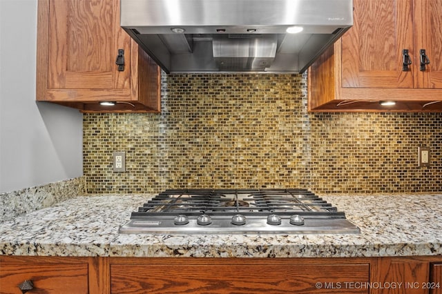 kitchen featuring tasteful backsplash, light stone countertops, exhaust hood, and stainless steel gas cooktop