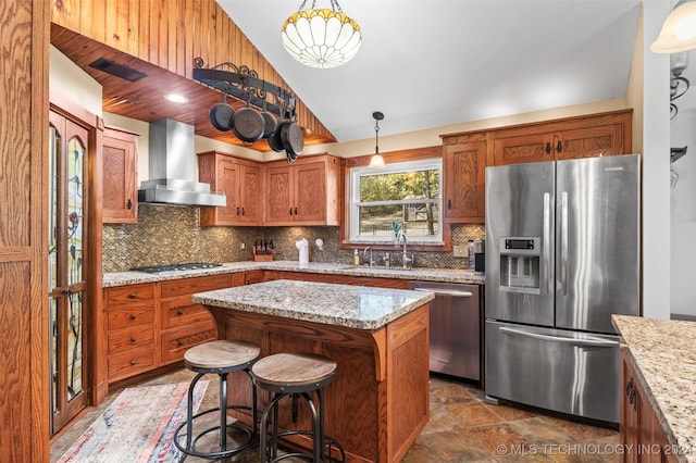 kitchen featuring appliances with stainless steel finishes, wall chimney exhaust hood, sink, pendant lighting, and a kitchen island