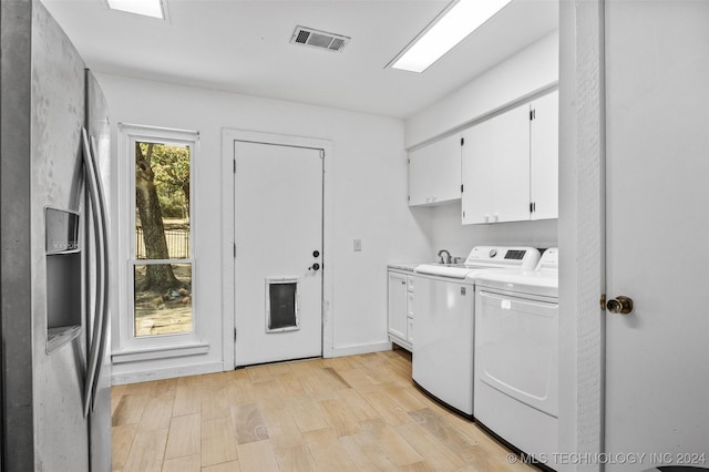 clothes washing area featuring cabinets, light hardwood / wood-style floors, and washer and clothes dryer