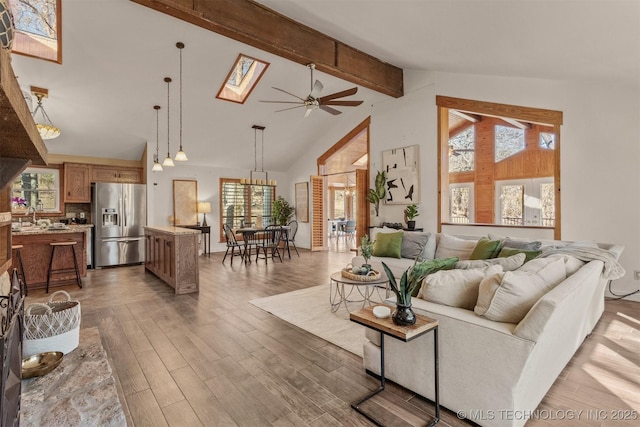 living area with a skylight, beam ceiling, a ceiling fan, wood finished floors, and high vaulted ceiling