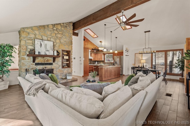 living room featuring light wood-style flooring, a fireplace, visible vents, and beam ceiling