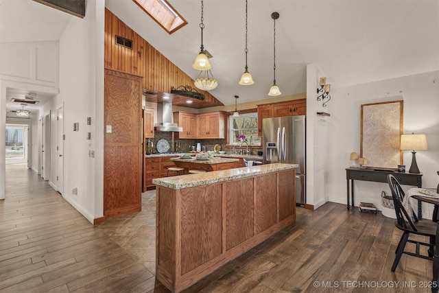 kitchen with a kitchen island, stainless steel fridge with ice dispenser, brown cabinets, wall chimney exhaust hood, and tasteful backsplash