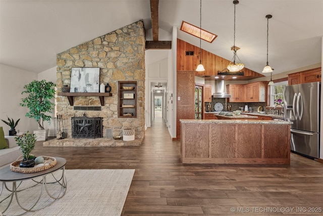 kitchen with stainless steel fridge, open floor plan, dark wood-style flooring, wall chimney range hood, and a fireplace