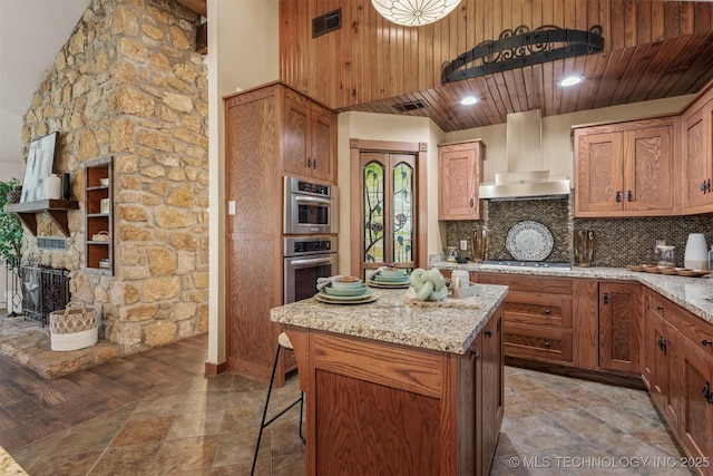 kitchen featuring visible vents, light stone counters, a center island, wall chimney range hood, and backsplash