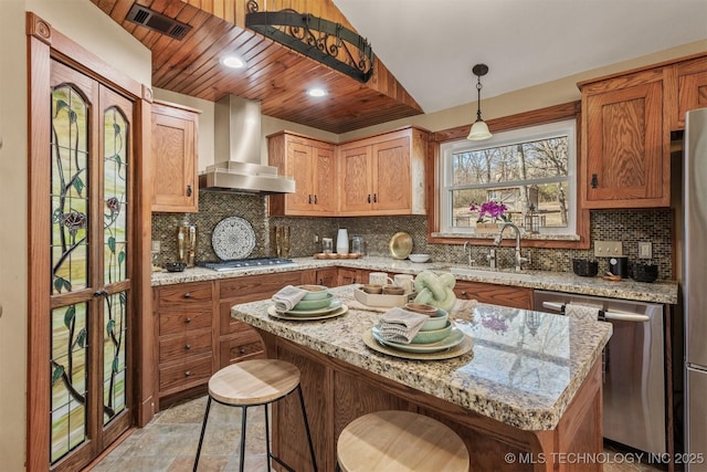 kitchen featuring stainless steel appliances, a sink, visible vents, backsplash, and wall chimney exhaust hood