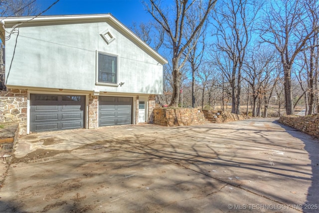 view of side of home featuring a garage, stone siding, driveway, and stucco siding