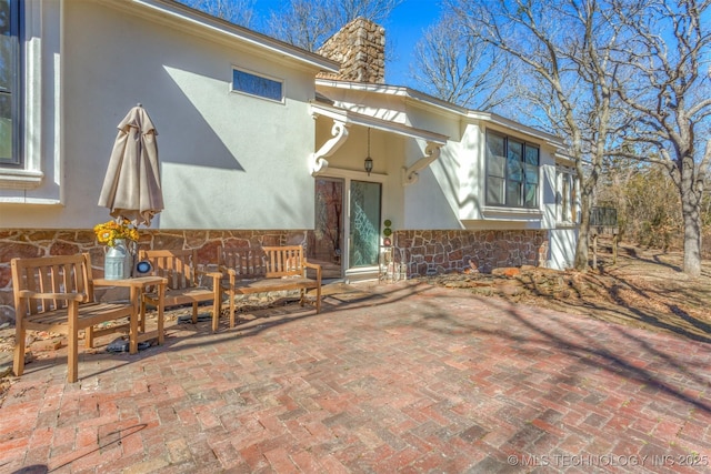 view of front facade featuring stone siding, a patio area, a chimney, and stucco siding