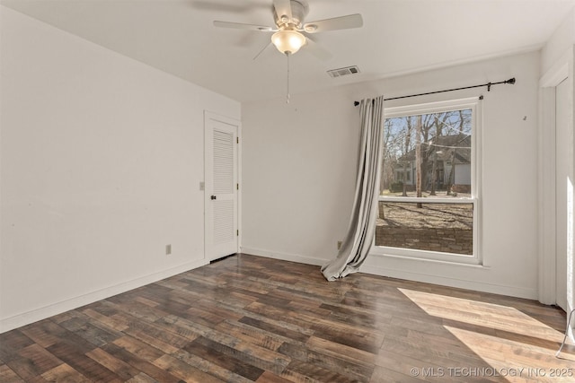 empty room featuring dark wood-style floors, a ceiling fan, visible vents, and baseboards