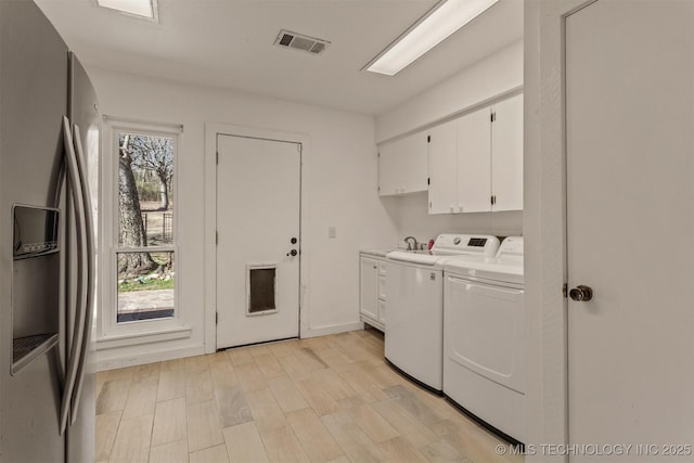 clothes washing area with separate washer and dryer, visible vents, baseboards, cabinet space, and light wood finished floors