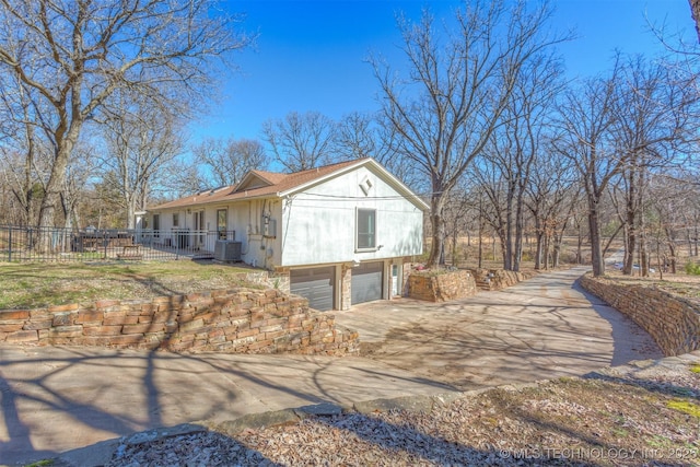 view of side of home with central air condition unit, an attached garage, fence, and concrete driveway