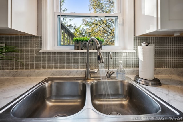 details with light stone countertops, white cabinetry, sink, and backsplash