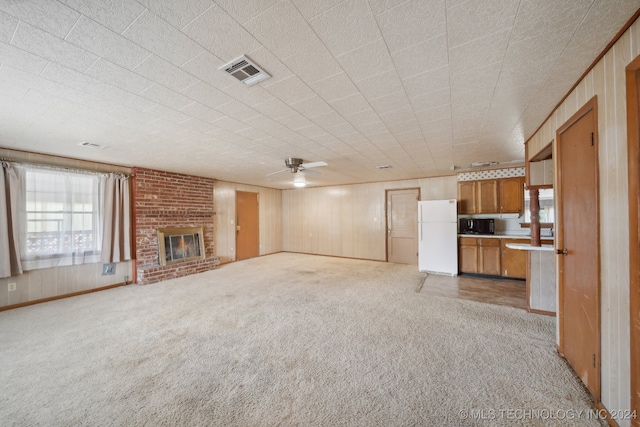 unfurnished living room with wood walls, a brick fireplace, light colored carpet, and ceiling fan