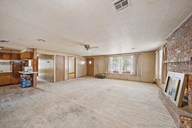 unfurnished living room with ceiling fan, brick wall, a fireplace, and light colored carpet