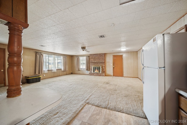 unfurnished living room featuring ceiling fan, carpet flooring, wooden walls, and a fireplace