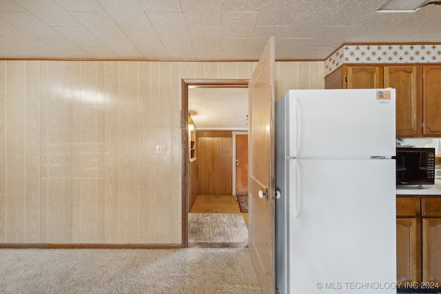 kitchen featuring white fridge, wood walls, and light colored carpet