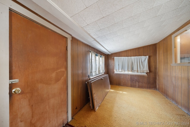 carpeted spare room featuring wooden walls and vaulted ceiling