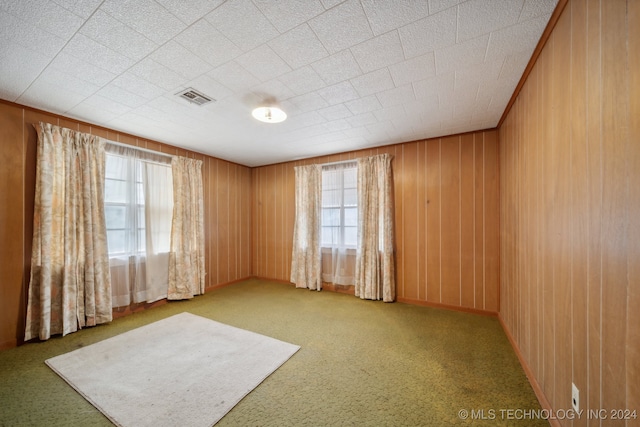 unfurnished room with a healthy amount of sunlight, light colored carpet, and wood walls