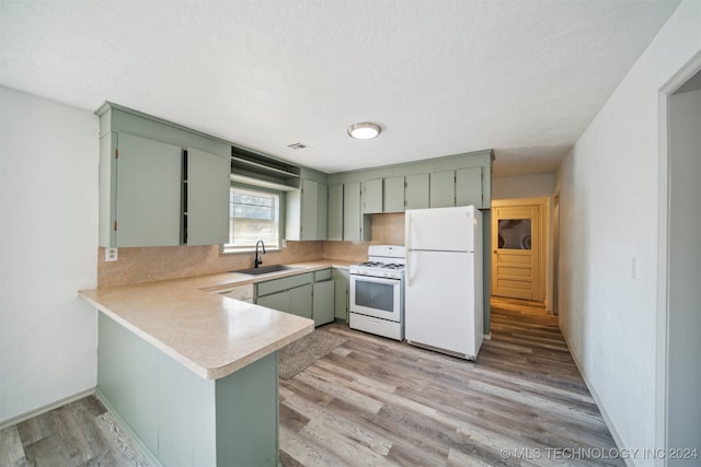 kitchen with white appliances, sink, light hardwood / wood-style floors, kitchen peninsula, and green cabinets