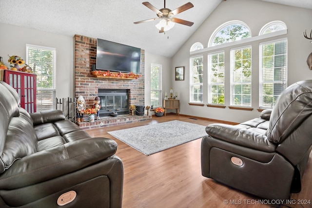 living room featuring a textured ceiling, a brick fireplace, light wood-type flooring, and ceiling fan