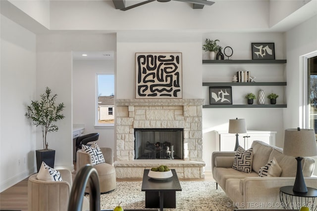 living room featuring hardwood / wood-style floors, ceiling fan, and a stone fireplace