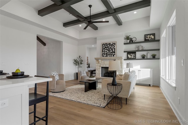 living room with a stone fireplace, ceiling fan, light hardwood / wood-style flooring, and beamed ceiling